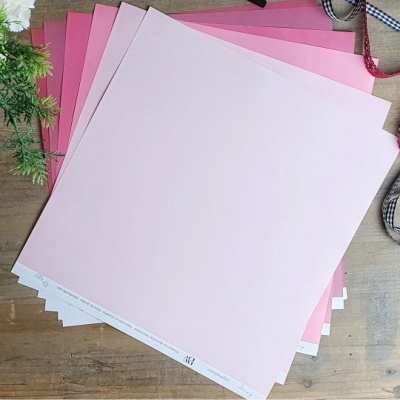 Folhas quadradas de papel rosa em vários tons sobre mesa de madeira com ramos e fitas