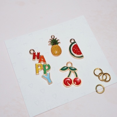 Pendentes esmaltados coloridos com motivos de frutas e palavra HAPPY sobre cartão branco