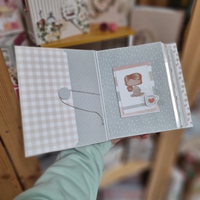 Álbum ou caderno aberto com ilustração de menina e chávena com coração em padrão cinza e bege.