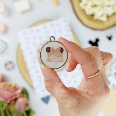 Pingente redondo com ilustração de menina com laço castanho e orelhas de rato.