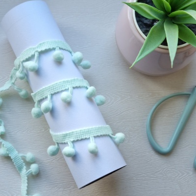 Rolo de tecido branco com fita com pompons verdes, planta suculenta e ferramenta azul