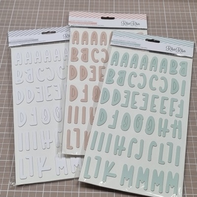 Autocolantes de letras em cartelas coloridas em tons pastel sobre mesa com padrão de grelha e cesta de vime