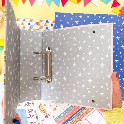 Pasta de argolas cinza com estrelas brancas aberta e mãos segurando