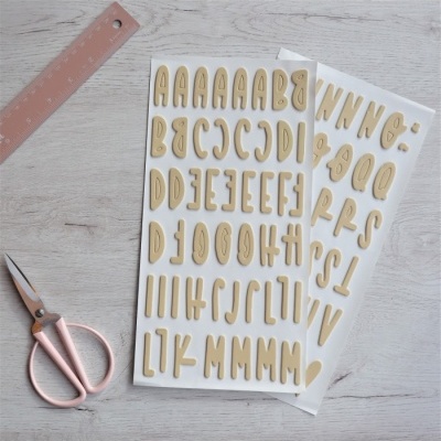 Cartazes com letras adesivas bege, régua rosa e tesoura rosa num fundo de madeira clara