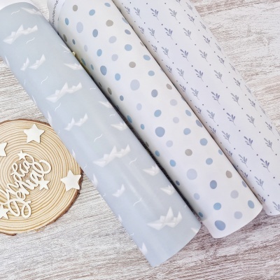 Três rolos de papel decorativo azul claro e branco com diferentes padrões sobre superfície de madeira