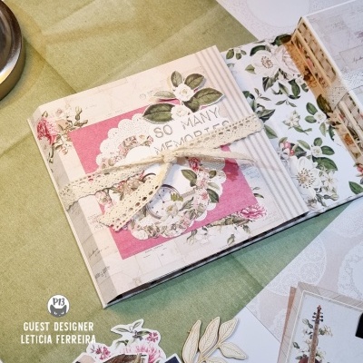 Livro decorativo com padrão floral e fita de renda sobre tecido verde claro