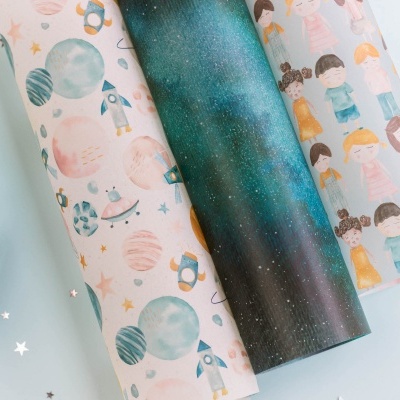 Três rolos de papel decorativo com temas espaciais e crianças em estilo cartoon sobre fundo claro