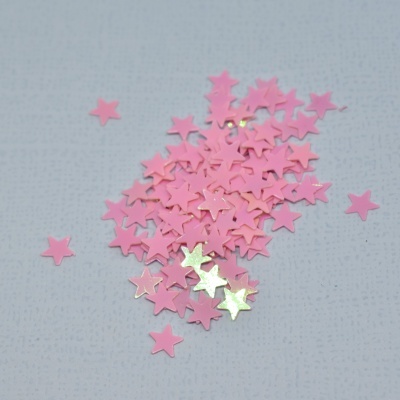 Brilhantes em forma de estrelas cor-de-rosa e douradas sobre superfície cinza