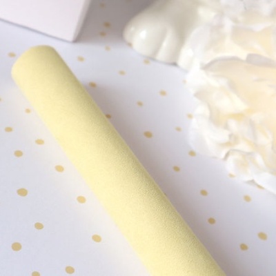 Rolo amarelo claro com textura suave sobre papel branco com pontos dourados e tecidos brancos ao fundo