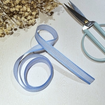 Fita têxtil azul e branca com padrão de riscas junto a tesoura azul clara e flores secas sobre mesa de madeira