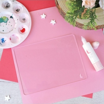 Tapete de silicone transparente com paleta de pintura, tubo branco e ornamentos brancos em fundo rosa