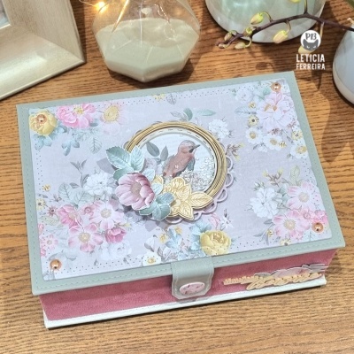 Caixa decorativa com padrão floral e adesivo de pássaro sobre mesa de madeira