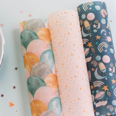 Três rolos de papel colorido com padrões variados em cima de uma superfície clara ao lado de um prato branco