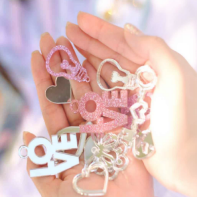 Chaveiros e bijuterias com corações e a palavra LOVE em rosa, branco glitter e prateado numa mão.
