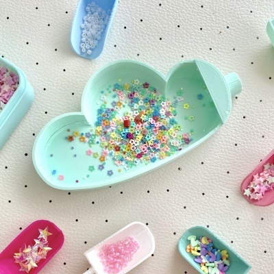 Bandejas coloridas com miçangas e ornamentos em superfície branca pontilhada.