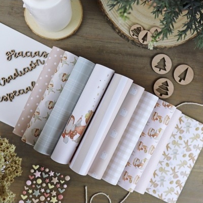 Rolos de papel decorativo em vários padrões e cores neutras dispostos numa mesa de madeira com decoração