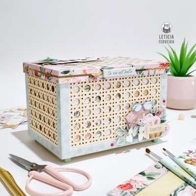 Caixa decorativa em rattan com decoração floral, etiqueta e objetos de escritório