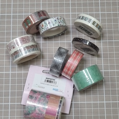 Rolos de fita de papel decorativa com vários padrões e cores sobre superfície quadriculada cinza