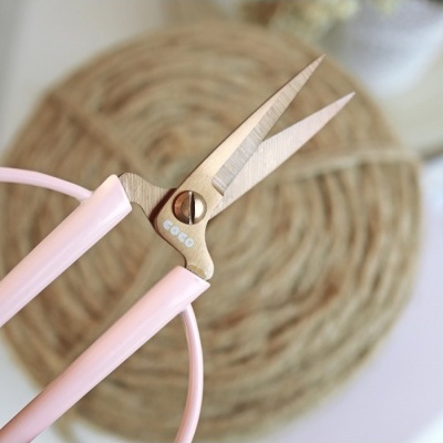 Tesoura metálica com cabo rosa claro e texto COCO próximo à articulação