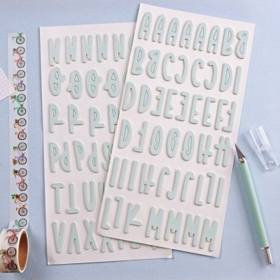 Folhas com autocolantes de letras maiúsculas azul claro, caneta e fita decorativa de bicicletas