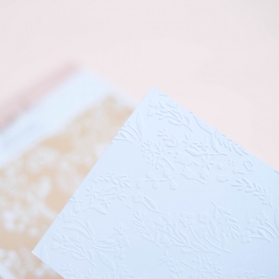 Folha branca com relevo floral sobre folha castanha clara, fundo rosa claro