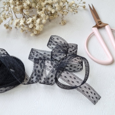 Fita de renda preta com padrão de bolinhas, ramo de flores secas e tesoura rosa