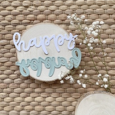 Recortes de palavra em placas sobre base de madeira com flores pequenas brancas, em fundo trançado bege.