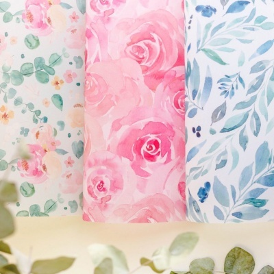 Tecidos florais dobrados em tons pastel sobre superfície clara com folhas