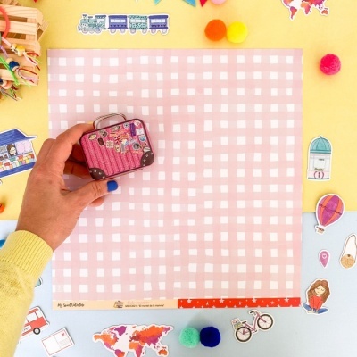 Miniatura de mala rosa com adesivos sobre pano xadrez rosa e branco com figuras recortadas ao redor