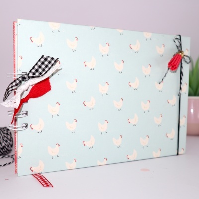 Caderno azul com padrão de galinhas brancas e decorações de tecido colorido