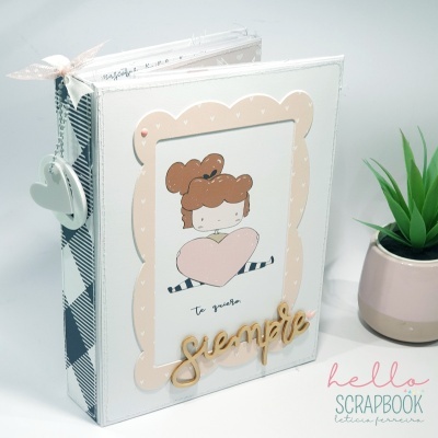 Álbum de scrapbook branco e bege com desenho e texto, ao lado vaso com planta artificial