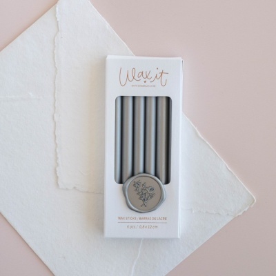 Pacote branco com seis velas cinzentas e selo cinzento com desenho floral e texto