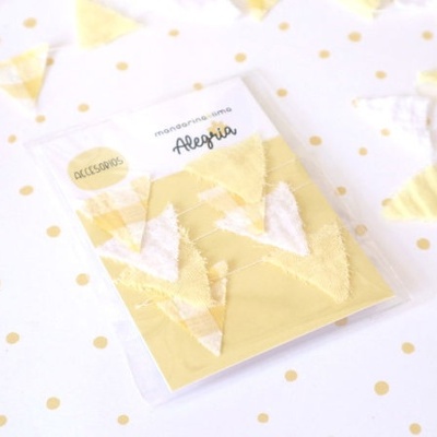 Acessórios em tecido amarelo e branco em embalagem com marca Alegria, fundo branco com pontos amarelos