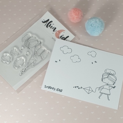 Conjunto de carimbos e cartão com desenho de menina, nuvens e papagaio, pompons rosa e azul sobre fundo rosa com corações.