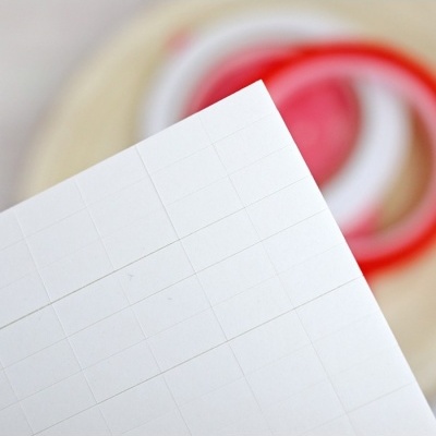 Folha branca com quadrículas e fitas adesivas desfocadas ao fundo
