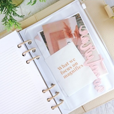 Caderno aberto com capa bege e bolso plástico contendo papéis com texto em inglês