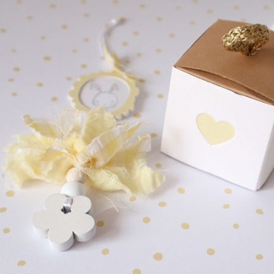 Caixa branca com tampa castanha e puxador de flor branca com tecido amarelo sobre fundo branco com pontos amarelos