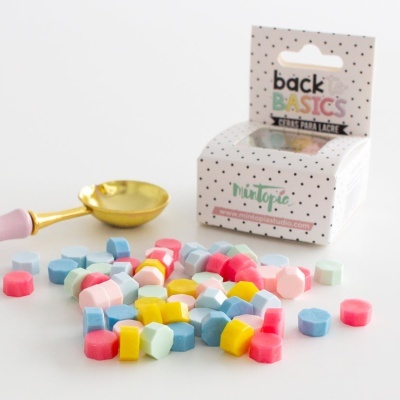 Velas hexagonais coloridas com colher dourada e caixa branca com texto