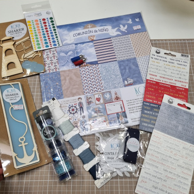 Materiais de scrapbook variados, incluindo papéis, adesivos, fitas e elementos decorativos, sobre mesa quadriculada