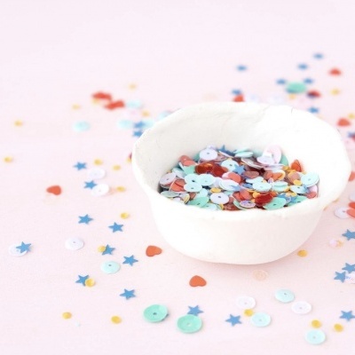taça branca com confetes coloridos sobre superfície rosa