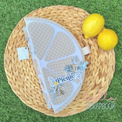 Caixa decorativa formato fatia de limão com padrão quadriculado e a palavra 'Picnic' junto a limões sobre esteira natural