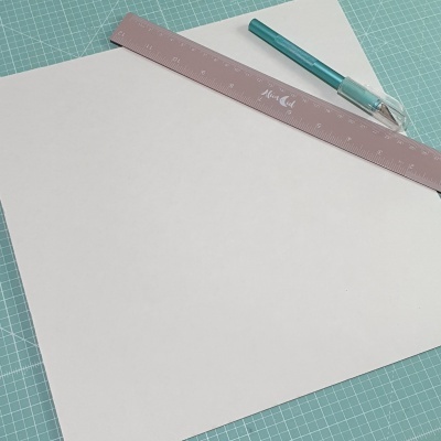 Folha de papel branca com régua rosa e caneta azul sobre base de corte verde