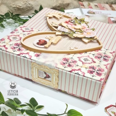 Embalagem decorativa retangular com padrão listrado rosa e flores, coração de madeira decorado e folhas verdes