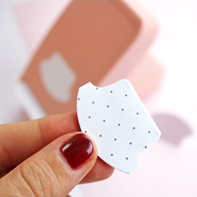 Peça branca com pontos pretos em mão com verniz vermelho, fundo desfocado cor de rosa