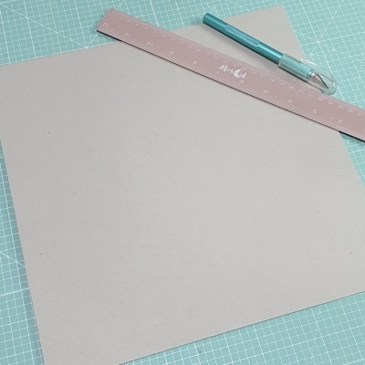 Folha de cartão cinza claro sobre tapete de corte com régua rosa e caneta azul