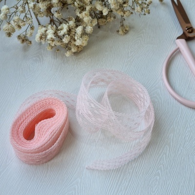 Fitas rendadas rosa claro com flores secas e tesoura rosa sobre superfície branca