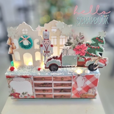 Decoração natalícia com casas, soldado, carro, flores e árvore em cima de caixa decorativa