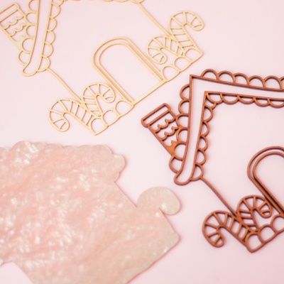 Estruturas em forma de casinha de materiais rosa fosco e arame bege e castanho sobre fundo rosa claro.