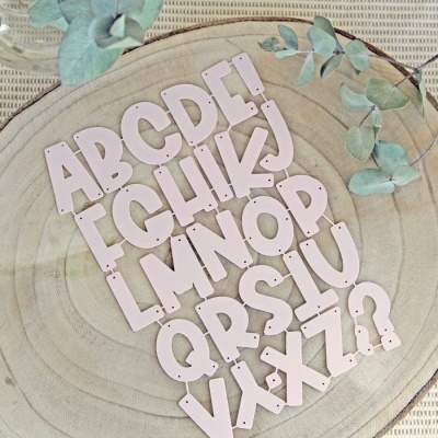 Letras do alfabeto em madeira rosa claro sobre base redonda de madeira clara com folhas secas verdes