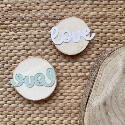 Elementos decorativos com a palavra love em letras cursivas sobre bases de madeira circular